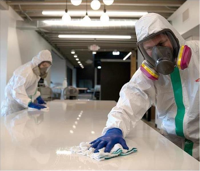 2 people wearing PPE cleaning a white commercial office table 
